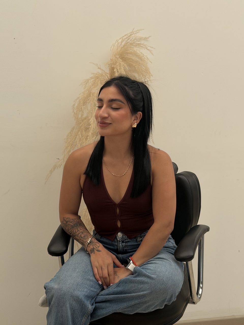 Retrato editorial de Camila Quiroga sentada frente a una pared neutra con plumas de pampa